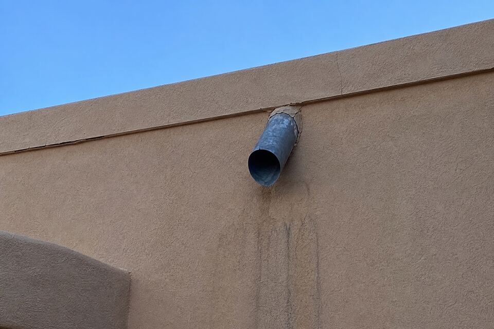 Santa Fe flat roof parapet with a metal canale and weathered stucco cap