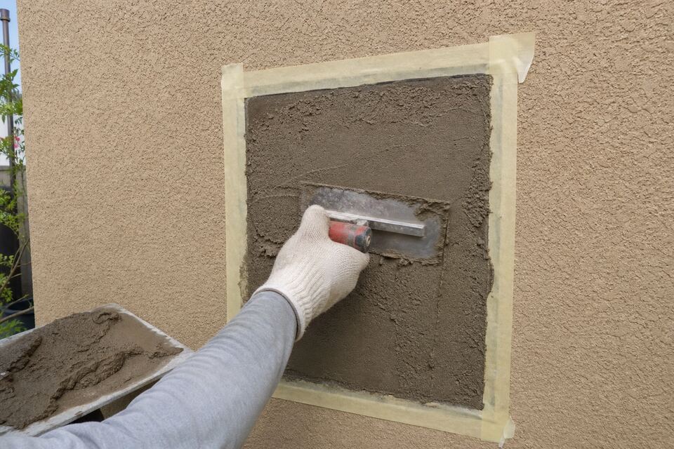 Trowel applying fresh stucco patch to a prepared section of wall